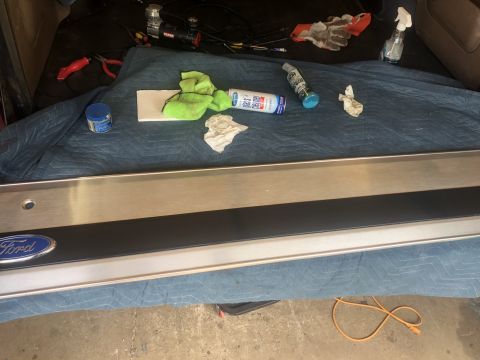 1995 Ford Bronco - Ford tailgate trim is laid out with cleaning supplies and tools, suggesting a repair or detailing process.