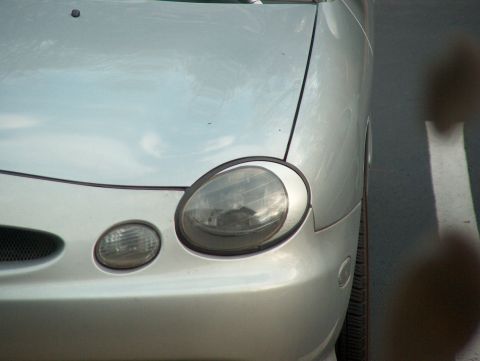 1998 Ford Taurus - Front corner of a silver 1998 Ford Taurus, showing the headlight and part of the grille.