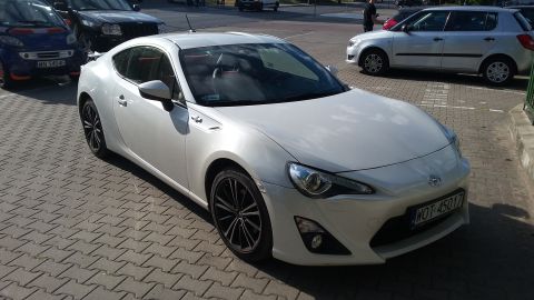White sports coupe parked on brick pavement. Other cars visible in background