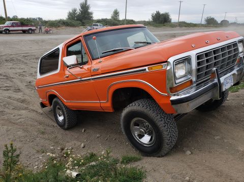 1978 Ford Bronco - This 1978 Ford Bronco is shown off-road, with other vehicles and people visible in the distance.