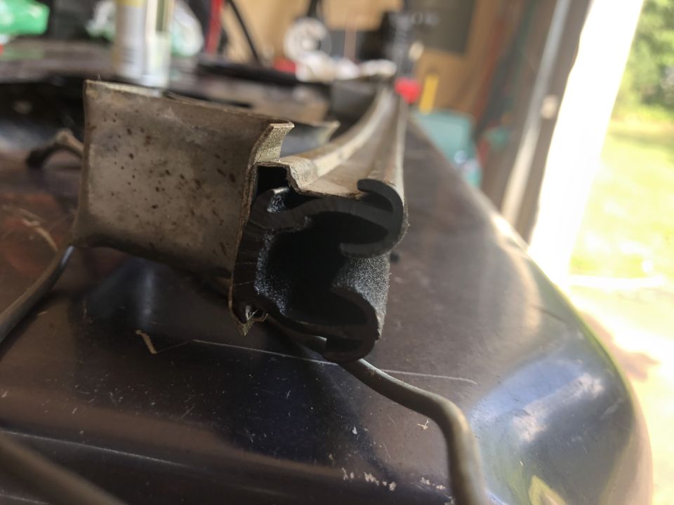 Close-up of a worn rubber seal with a metal bracket attached, resting on a dark surface