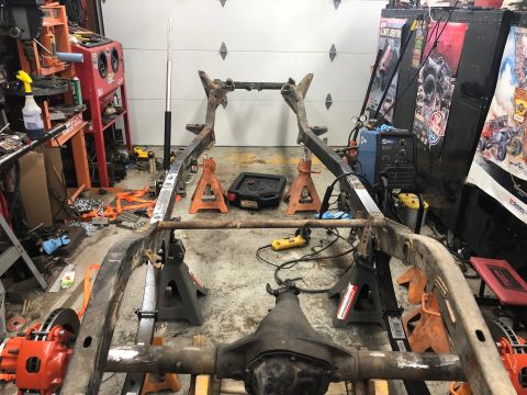 1992 Jeep Wrangler - A vehicle frame is supported by jack stands in a workshop, with tools and equipment visible in the background.