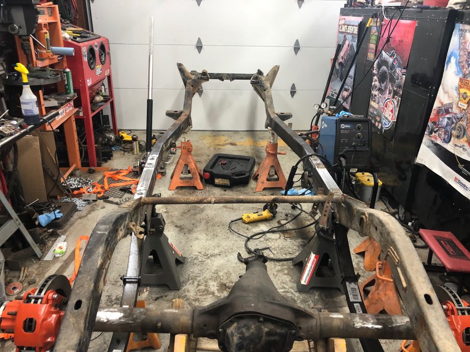 Vehicle frame on jack stands in a garage, showing rust and some new welds