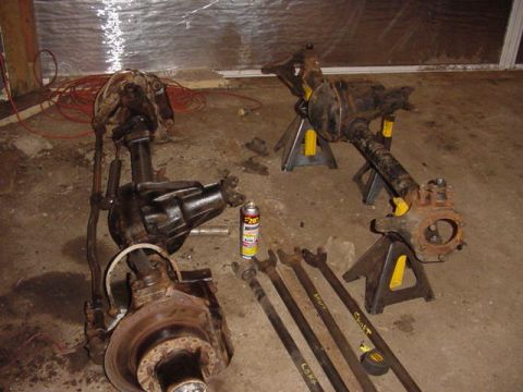 1992 Ford Bronco - Vehicle axles and driveshafts are displayed on jack stands and the floor, ready for work.