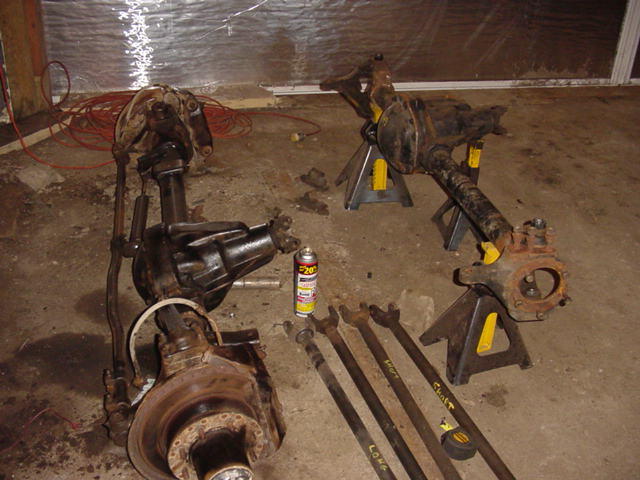 Several vehicle axles and driveshafts laid out on a concrete floor with a can of spray lubricant