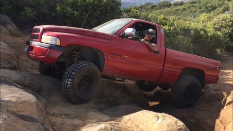 1996 Dodge 1500 - A red Dodge Ram pickup truck navigates a rocky off-road trail with a driver behind the wheel.