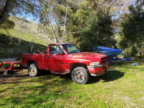 1996 Dodge 1500 - A red pickup truck is parked outdoors on a sunny day, with a boat on a trailer behind it.