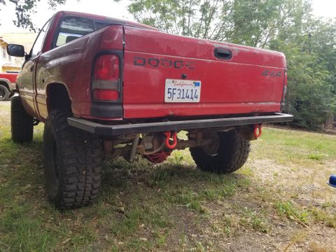 1996 Dodge 1500 - This red Dodge pickup truck features a custom rear bumper and is lifted with large off-road tires.