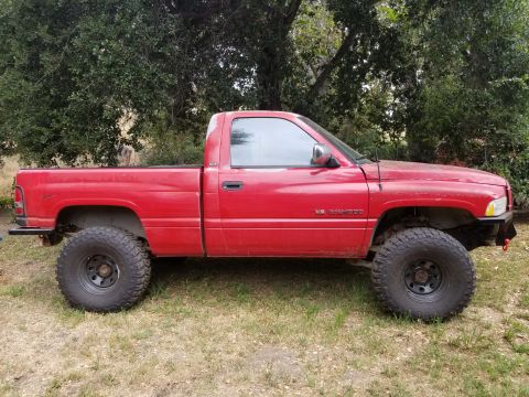 1996 Dodge 1500 - This red 1996 Dodge 1500 pickup truck features a lifted suspension and oversized tires, presented in a side profile view.