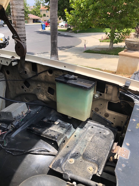 1981 Ford Bronco - The engine bay of a 1981 Ford Bronco is visible, with a coolant reservoir and hood hinge in view.