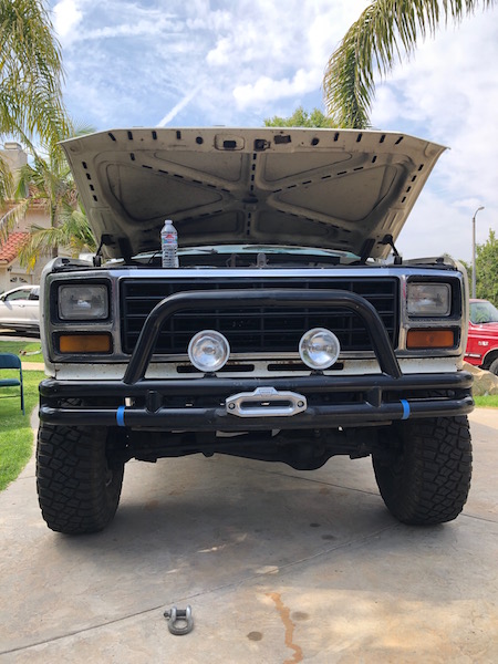 1981 Ford Bronco - A white Ford Bronco is parked with its hood open, showing an aftermarket bull bar and off-road tires.