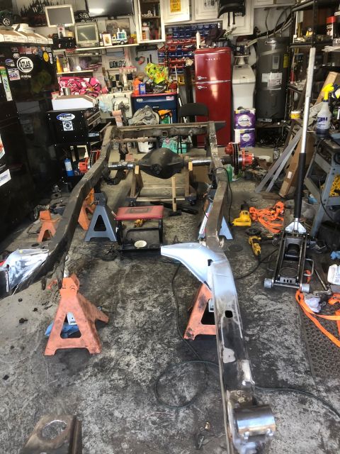 1992 Jeep Wrangler - The frame of a Jeep Wrangler is disassembled and supported by jack stands in a workshop.