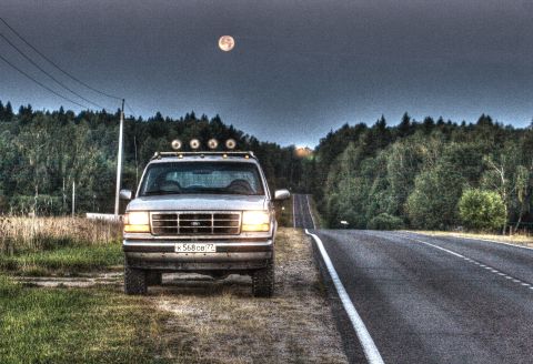 1993 Ford Bronco - A 1993 Ford Bronco is parked on the side of a road under a full moon, with a forest in the background.