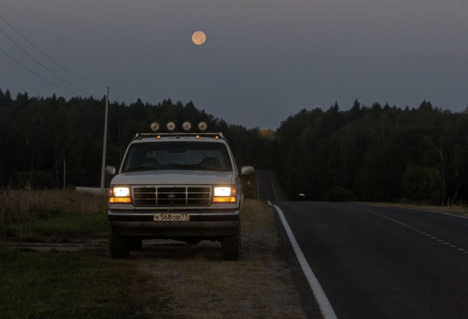 Ford Bronco parked on dirt shoulder next to a road, full moon in the sky