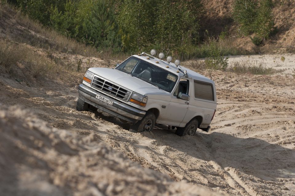 White Ford Bronco driving up a sandy hill. It has four lights on the roof rack