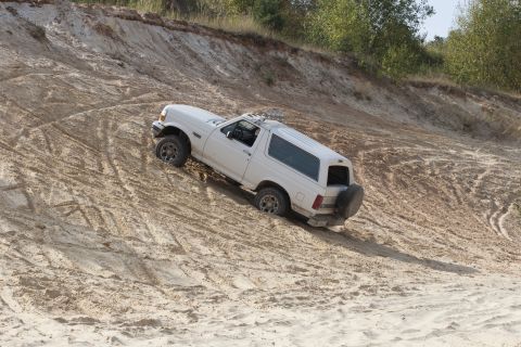 1993 Ford Bronco - White SUV navigates a steep sand dune, showing its rear-mounted spare tire.