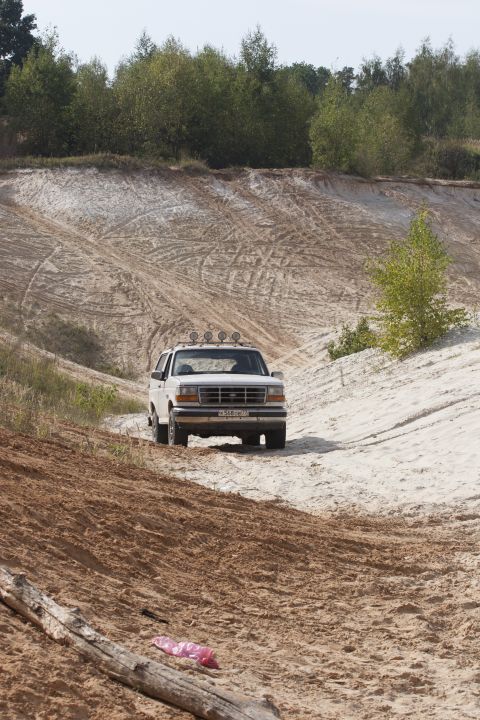 1993 Ford Bronco - A white Ford Bronco navigates a sandy terrain, its front grille and headlights clearly visible.