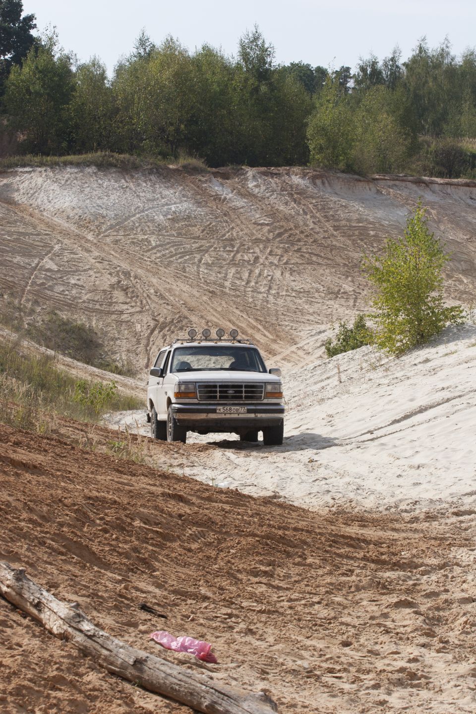 White Ford Bronco driving on a sandy hill, front view. It has four lights on the roof rack