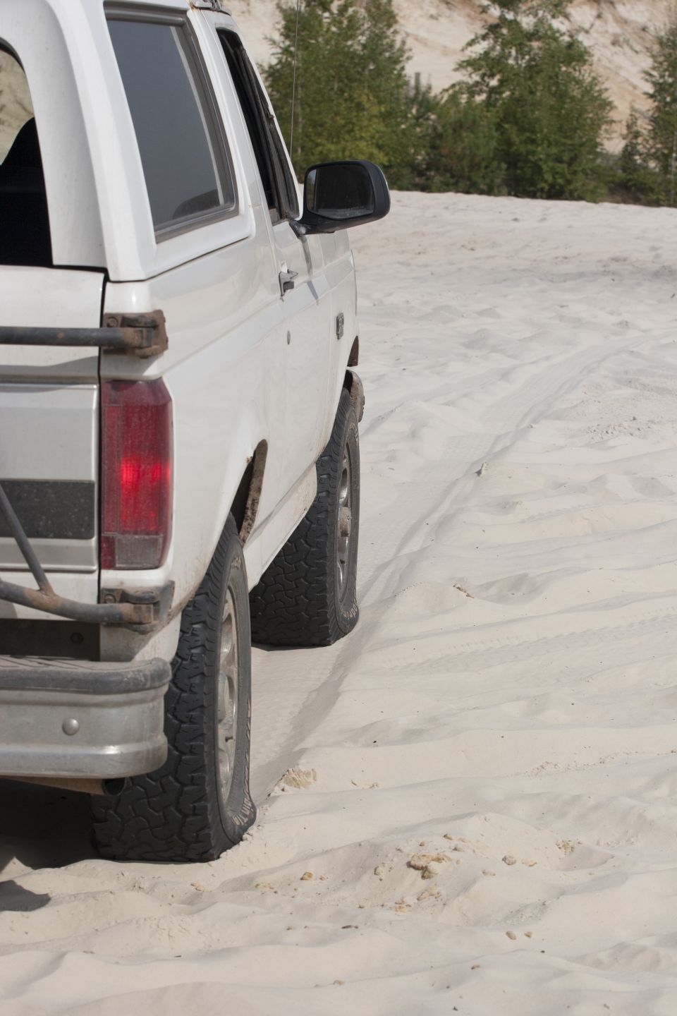 1993 Ford Bronco side view, driving on a sandy terrain with trees in the background
