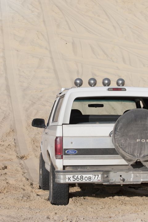 1993 Ford Bronco - The rear of a white Ford Bronco is visible as it drives on a sandy terrain, equipped with roof-mounted lights.