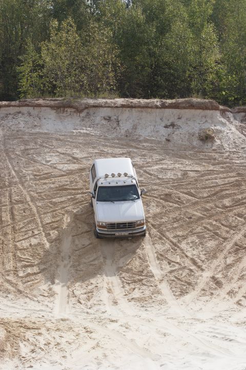 1993 Ford Bronco - White 1993 Ford Bronco navigates a sandy incline, leaving tire tracks in its wake.