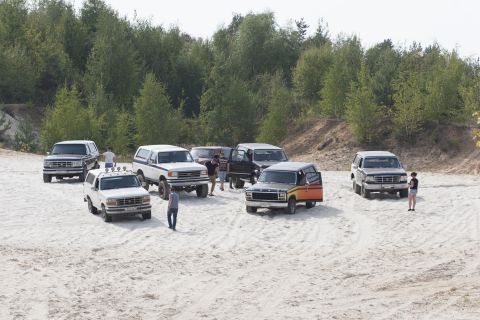 1993 Ford Bronco - Multiple Ford Bronco SUVs are gathered in a sandy outdoor location with trees.
