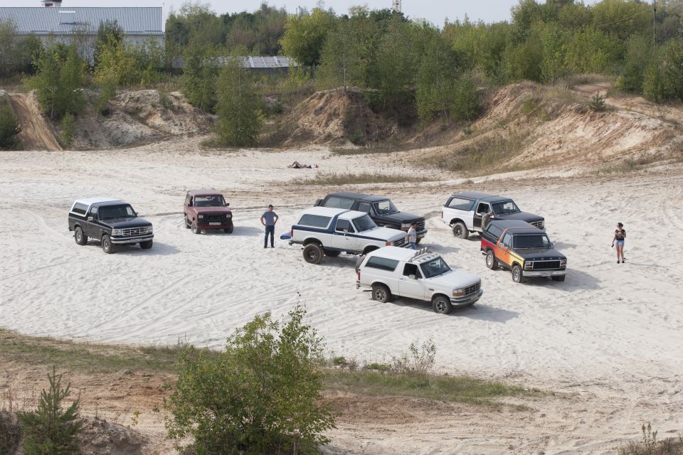 Several Ford Bronco SUVs parked on a sandy lot with some people standing around