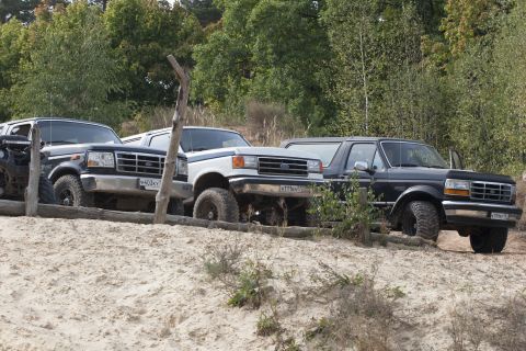 1993 Ford Bronco - Three Ford Broncos are parked on a sandy incline, with trees in the background.