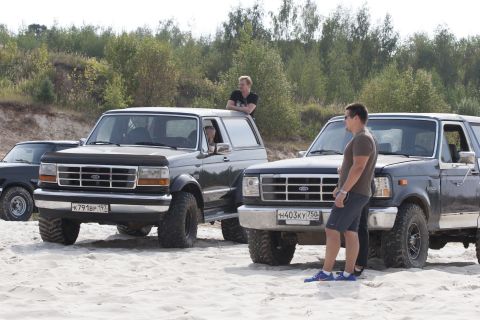 1993 Ford Bronco - Multiple Ford Bronco SUVs are parked on a sandy area with trees in the background.