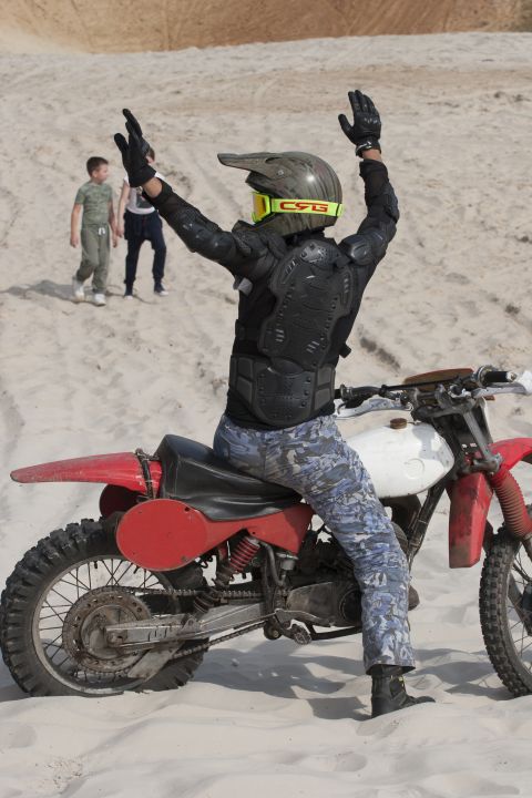 1993 Ford Bronco - A person in full gear sits on a dirt bike with arms raised in a sandy landscape.