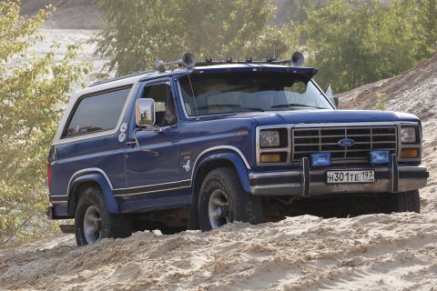1993 Ford Bronco - This blue Ford Bronco features a white roof, aftermarket lights, and a distinctive horse emblem on its side.