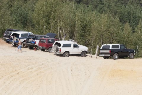 1993 Ford Bronco - Multiple Ford Bronco SUVs are parked on a sandy terrain with a wooded area behind them.