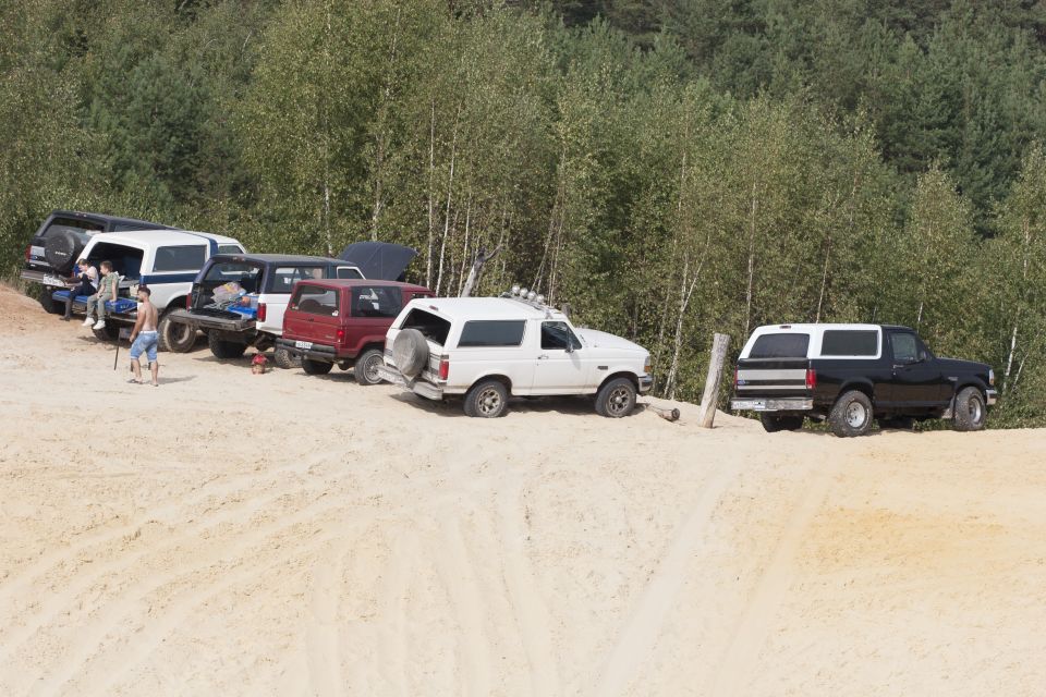Several Ford Bronco SUVs parked on a sandy area with trees in the background. One white Bronco has a spare tire on the back
