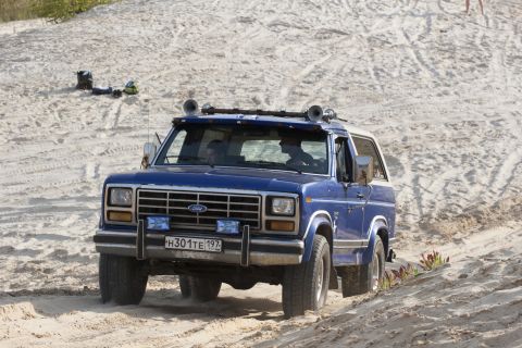 1993 Ford Bronco - This blue Ford Bronco is driving on a sandy terrain, kicking up dust.