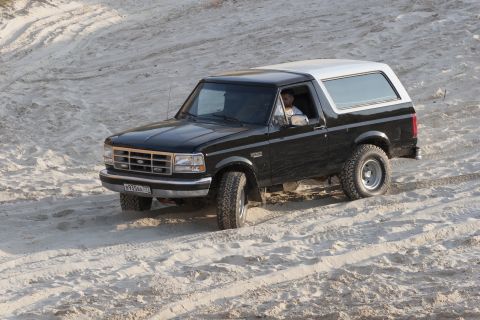 1993 Ford Bronco - A black 1992 Ford Bronco with a white top navigates a sandy landscape.
