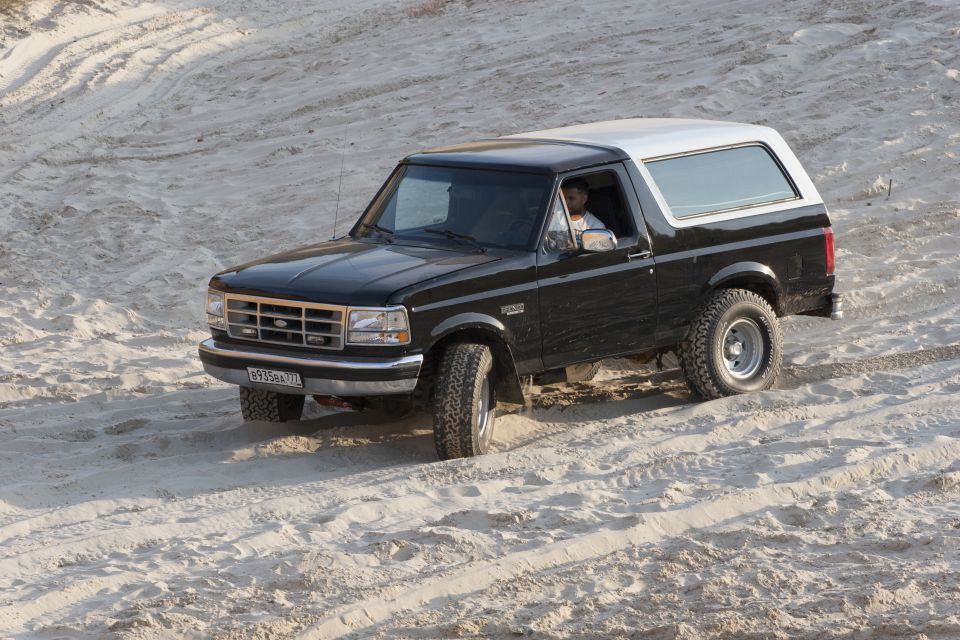 Black 1992 Ford Bronco with a white removable top driving on a sandy terrain, front-left view