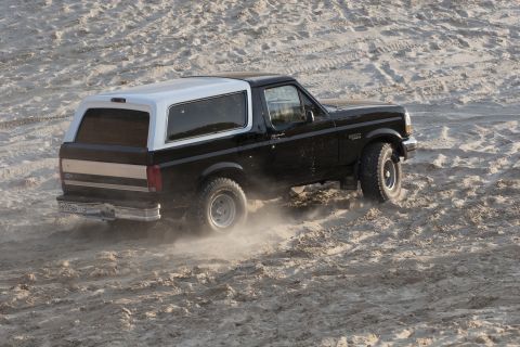 1993 Ford Bronco - A black and white 1993 Ford Bronco kicks up sand as it drives across a sandy terrain.
