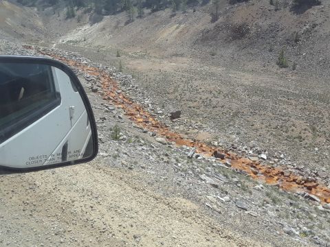 1999 Ford E250 - View from a white van's side mirror shows a desolate, rocky terrain with a dry streambed stained orange.
