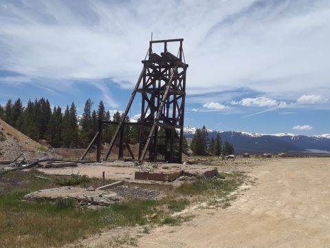 1999 Ford E250 - A wooden mine headframe stands against a backdrop of snow-capped mountains and a blue sky with scattered clouds.