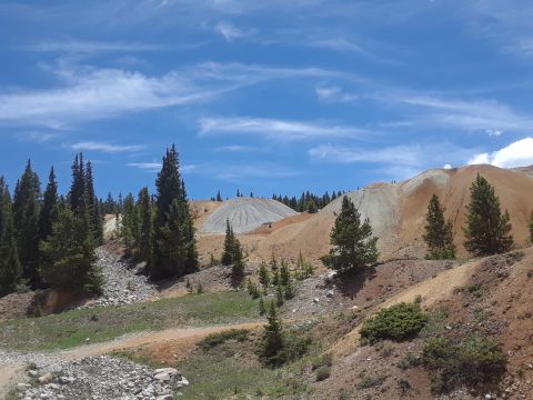 1999 Ford E250 - A scenic view of a mining area with distinct piles of earth and scattered evergreen trees under a bright blue sky with wispy clouds.