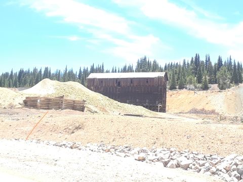1999 Ford E250 - An old mine building stands against a backdrop of trees, with large piles of excavated material in the foreground.