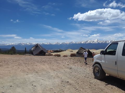 1999 Ford E250 - A white van is parked on a dirt road with abandoned structures and mountains in the distance.