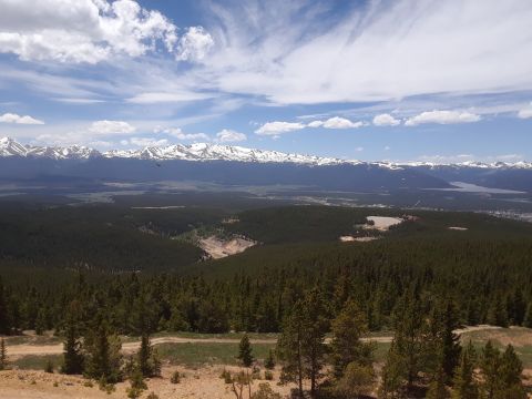 1999 Ford E250 - Expansive mountain landscape with snow-capped peaks, dense forest, and a clear blue sky.