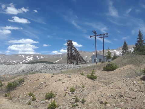 1999 Ford E250 - A wide view of an abandoned mine site with a wooden headframe and industrial buildings under a blue sky.