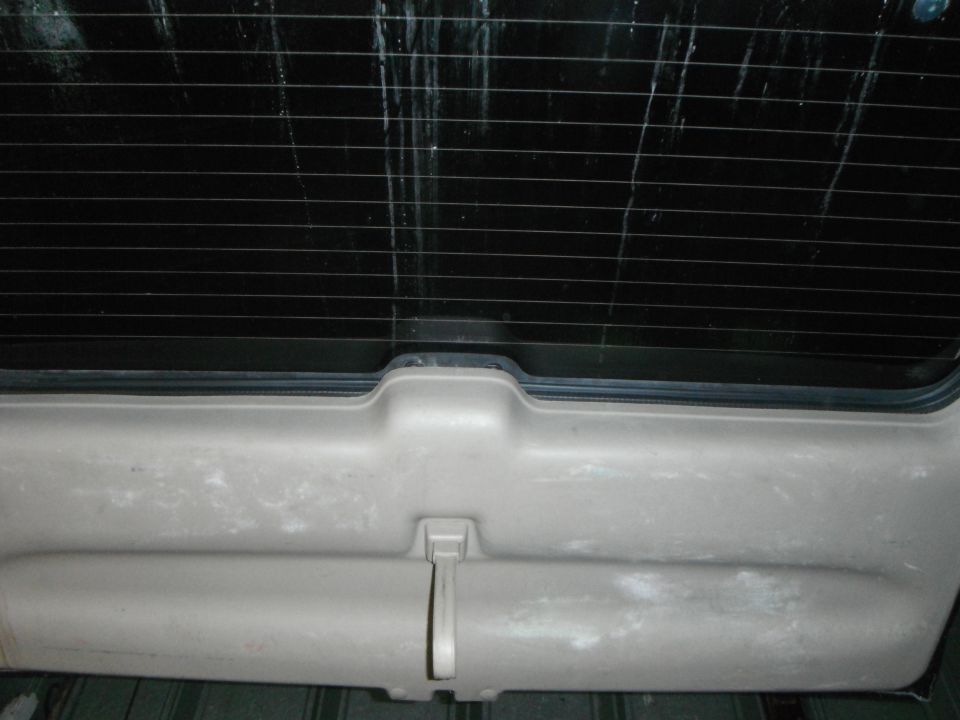 Tan plastic interior panel below a black rear window with horizontal defroster lines. A light-colored handle is visible