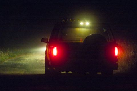 1993 Ford Bronco - A rear view of an SUV driving on a road at night, with its brake lights and roof lights illuminated.