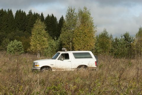 1993 Ford Bronco - White 1993 Ford Bronco navigates a field with trees in the background under a cloudy sky.