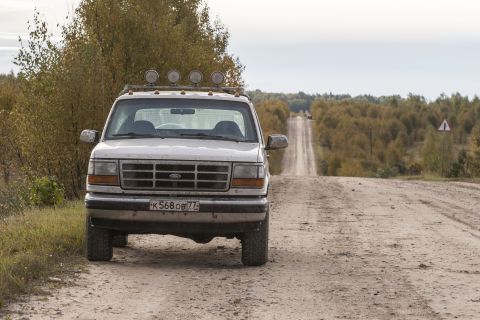 1993 Ford Bronco - A white Ford Bronco is parked on a dirt road, with a long, straight road stretching into the distance.