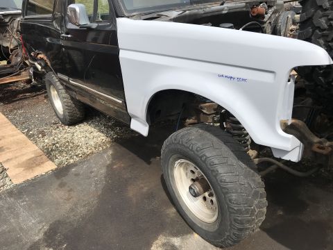 1992 Ford Bronco - A 1992 Ford Bronco's front fender is painted white, contrasting with the black body, and shows blue text indicating the engine type.