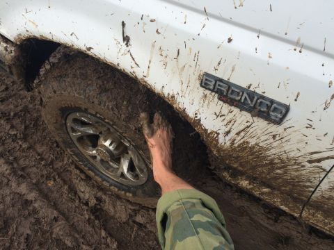 1993 Ford Bronco - A foot is stuck in the mud next to the wheel of a white 1993 Ford Bronco.